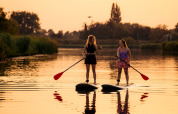 Due donne su paddleboard al tramonto su un lago calmo, immerse nella natura vicino a un glamping.