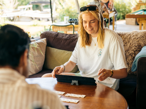 Young woman plays a board game with a friend inside a cozy glamping accommodation, smiling happily.