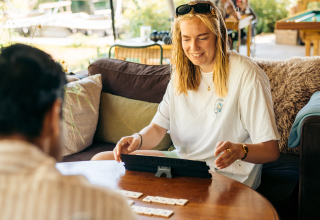 Jonge vrouw speelt een gezelschapsspel met een vriend in een sfeervolle glampingaccommodatie.