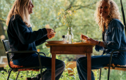 Two women sit at a table enjoying a meal together at a glamping accommodation, surrounded by greenery.
