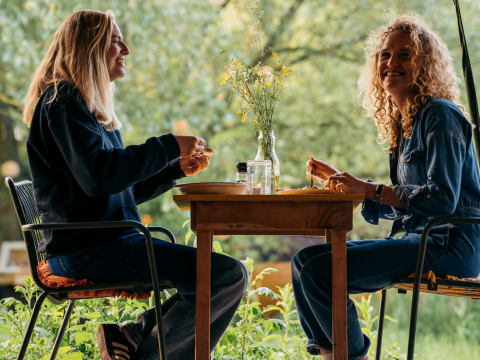 Deux femmes dînent ensemble à une table lors d’un séjour glamping entourées de verdure et de nature.