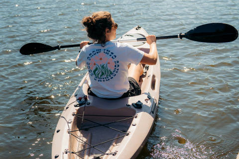Persona remando en kayak bajo el sol en aguas tranquilas, vista trasera, tomada en un alojamiento glamping.