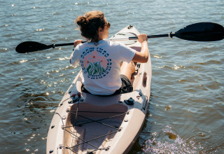 Persona remando en kayak bajo el sol en aguas tranquilas, vista trasera, tomada en un alojamiento glamping.