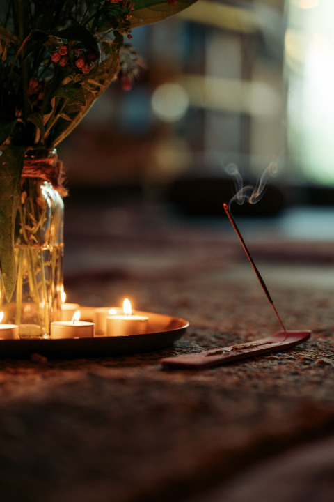 Ambiente de glamping con velas encendidas, flores en jarrón de vidrio y varilla de incienso humeante.