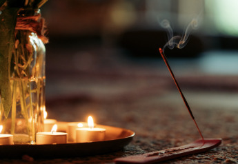 Ambiente de glamping con velas encendidas, flores en jarrón de vidrio y varilla de incienso humeante.