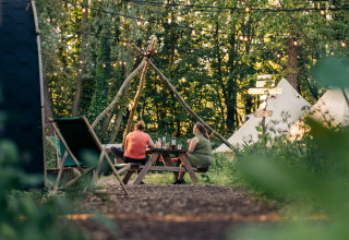 Dos personas sentadas en una mesa de picnic en un camping glamping rodeado de tiendas y luces.