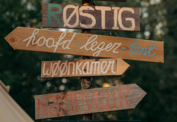 Handbeschilderde houten borden met Nederlandse tekst bij een glamping, omringd door groene natuur.