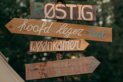 Handgemachte Holzschilder mit niederländischem Text bei einer Glamping-Unterkunft im Grünen.