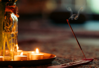 Cozy glamping setup with lit candles and incense stick emitting smoke, creating a relaxing atmosphere.