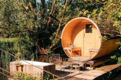 Hébergement glamping extérieur avec cabane en bois en forme de baril et baignoire entourée de verdure.