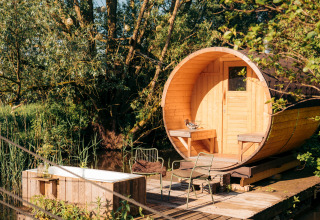 Outdoor glamping accommodation with a round wooden barrel cabin and bathtub surrounded by lush greenery.