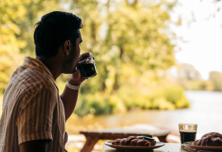 Un hombre toma café en una mesa al aire libre con pasteles, disfrutando vistas naturales en un glamping.