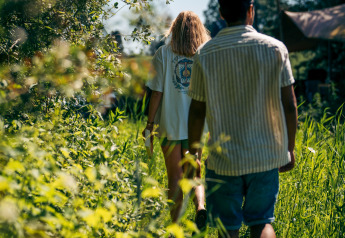 Dos personas caminan entre plantas verdes hacia un alojamiento glamping en un día soleado de verano.