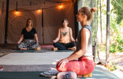Donne praticano meditazione su tappetini yoga in una tenda glamping decorata con luci soffuse.