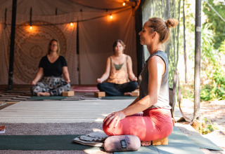 Mujeres meditan sobre esterillas de yoga en una carpa glamping decorada con luces cálidas.
