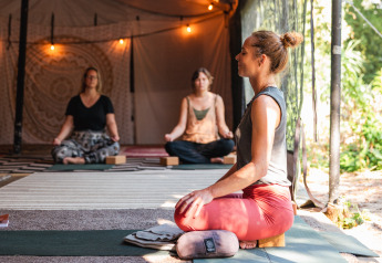 Mujeres meditan sobre esterillas de yoga en una carpa glamping decorada con luces cálidas.