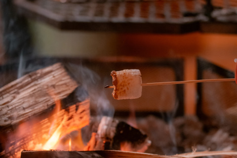 Un marshmallow viene tostato su un fuoco da campo in un ambiente accogliente di glamping di lusso.