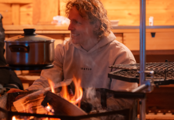 Una persona se sienta en una cabaña de madera junto al fuego con una olla, disfrutando de glamping.
