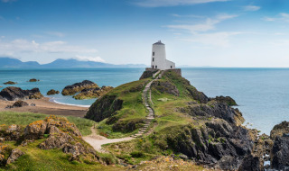 Un sendero serpenteante conduce a un faro blanco junto al mar cerca de Bala, Gales, con costa rocosa y vistas.