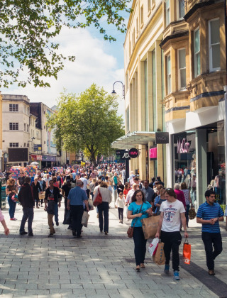 Calle comercial concurrida con multitudes, tiendas y árboles cerca de Bala, Gales, Reino Unido, en un día soleado.