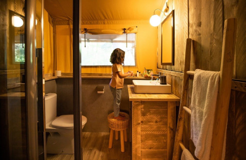 Child stands on a stool in the bathroom of GlampCamp Safari Tent at Camping De Klimberg, Netherlands.