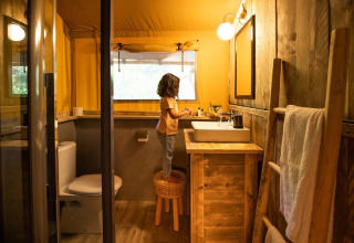 Bambino in piedi su uno sgabello nel bagno della GlampCamp Safari Tent al Camping De Klimberg, Paesi Bassi.