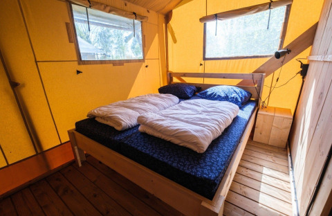 Interior de la tienda GlampCamp Safari en Camping De Klimberg, Países Bajos, con una cómoda cama doble.