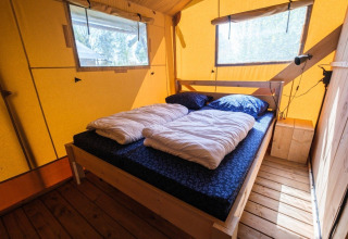 Interior de la tienda GlampCamp Safari en Camping De Klimberg, Países Bajos, con una cómoda cama doble.
