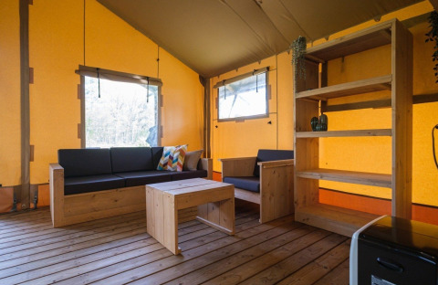 Vista interior de una tienda safari GlampCamp en Camping De Klimberg, Países Bajos, con muebles de madera.