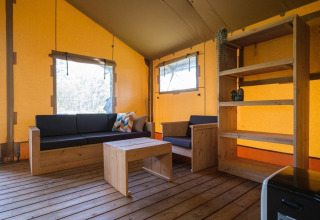 Vista interior de una tienda safari GlampCamp en Camping De Klimberg, Países Bajos, con muebles de madera.