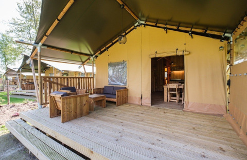 Terraza exterior y entrada de la tienda GlampCamp Safari Tent en Camping De Klimberg, Países Bajos, con muebles de madera.