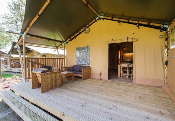 Buitenveranda en ingang van de GlampCamp Safari Tent op Camping De Klimberg in Nederland, met houten meubels.