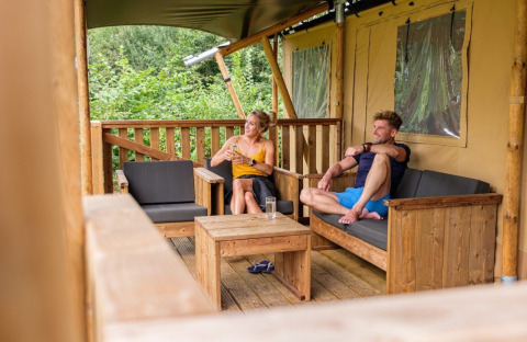 Deux personnes se détendent sur la terrasse d'une tente safari au GlampCamp Safari Tent à Camping De Klimberg, Pays-Bas.