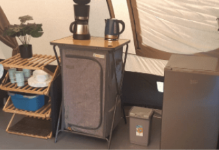 Køkkenområde i en De Waard tunnel telt med hylde, kaffemaskine, elkedel og et lille køleskab.