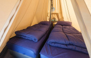 Interior of a De Waard tunnel tent with two single beds, cozy blue duvets and pillows for a safari stay.