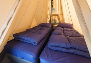 Intérieur d'une tente tunnel De Waard avec deux lits simples, couettes bleues et ambiance safari confortable.