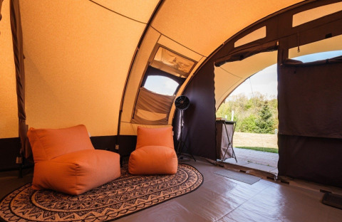 Interieur van een De Waard safaritent met gezellige stoelen en zicht op de groene buitenomgeving.