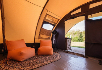 Interieur van een De Waard safaritent met gezellige stoelen en zicht op de groene buitenomgeving.