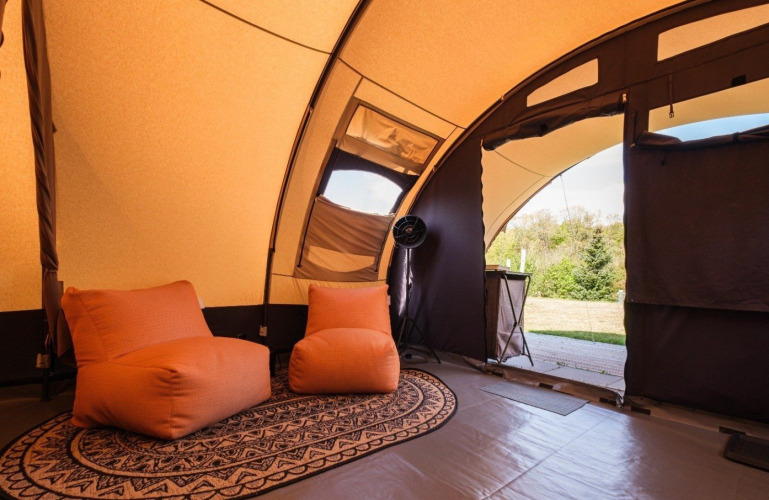Binnenkant van een De Waard safari tunnel tent met comfortabele stoelen en uitzicht op het groen.