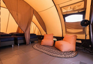 Interno di una tenda tunnel De Waard con letti comodi, poltrone arancioni e tappeto decorativo.