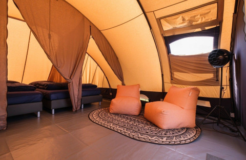 Interno di una tenda tunnel De Waard con letti comodi, poltrone arancioni e tappeto decorativo.