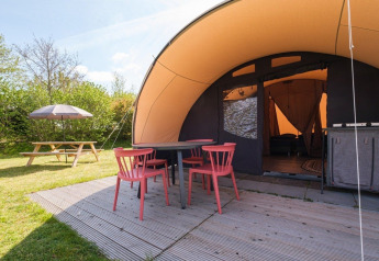 Buitenruimte bij De Waard tunnel tent met rode stoelen, tafel op vlonder en picknickbank op het gras.