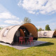 Safari telte på en campingplads under en blå himmel med grøn græsplæne og udendørs siddeplads foran teltet