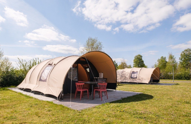 Safaritenten op een camping onder een blauwe lucht met groen gras en zitplek voor de tent