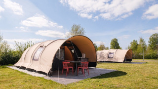 Safari tents at a campsite under a blue sky with green grass and outdoor seating area in front of the tent