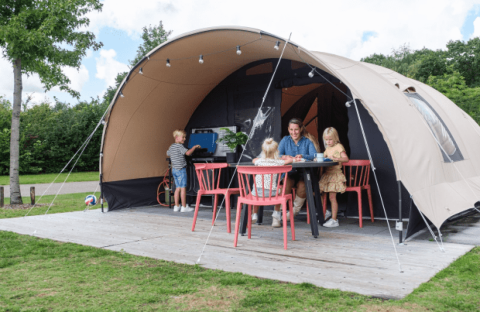 Familia disfruta frente a una tienda safari De Waard tipo túnel, niños jugando y adultos sentados en la mesa.