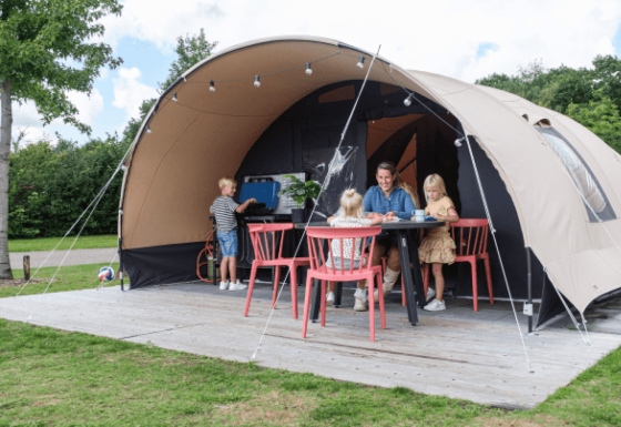 Familia disfruta frente a una tienda safari De Waard tipo túnel, niños jugando y adultos sentados en la mesa.