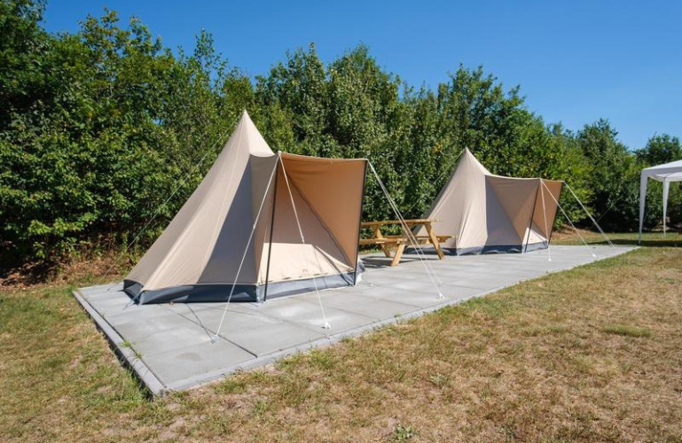 Dos tiendas túnel safari De Waard en Camping De Klimberg, Países Bajos, sobre suelo pavimentado y mesa.