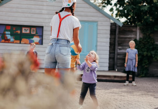 Niños juegan al aire libre en un alojamiento glamping, una adulta interactúa con una niña frente a una cabaña.
