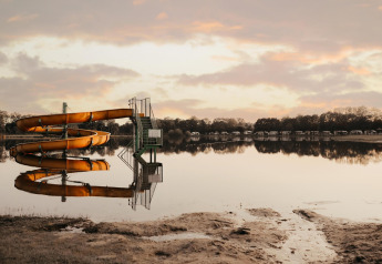 Scivolo d’acqua vicino a un lago calmo con riflessi e tende glamping sullo sfondo all’alba o al tramonto.